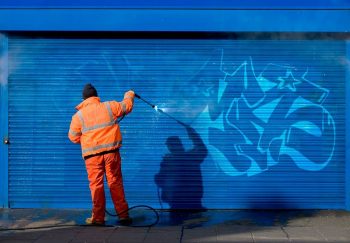 a man removes graffiti from commercial storefront