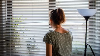 A woman looking out of her window blinds in her home